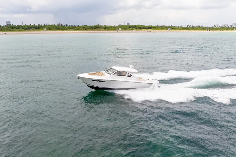The Image of 2018 Pursuit DC 365 Dual Console cruising on open water near a sandy shoreline. - 5