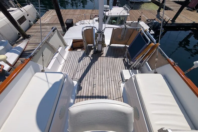 Slide: The Image of 1987 Island Gypsy 32 boat deck with wooden flooring and cushioned seating at a marina. - 28