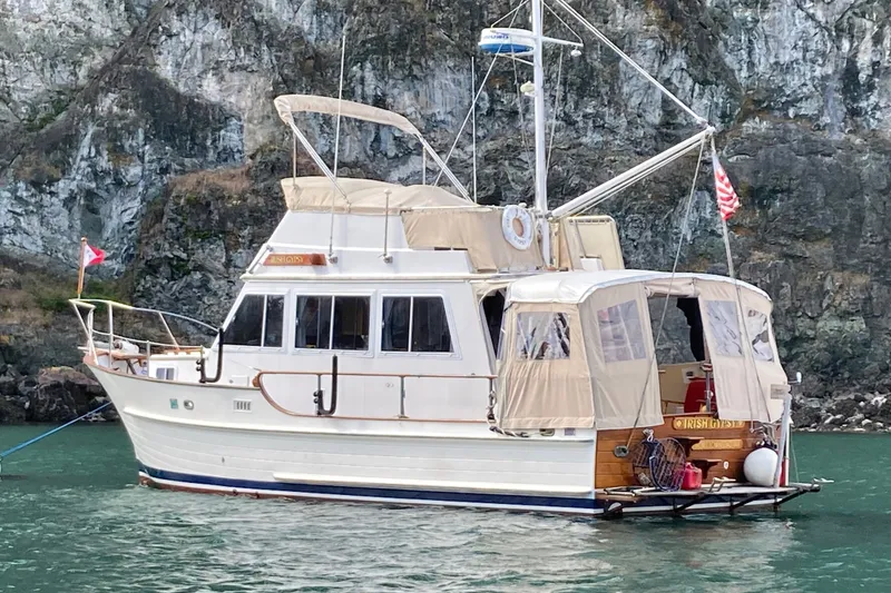 The Image of 1987 Island Gypsy 32 boat anchored near rocky cliffs in calm waters. - 0