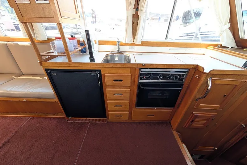 Slide: The Image of 1987 Island Gypsy 32 yacht kitchen with wooden cabinetry, stove, sink, and seating area. - 10