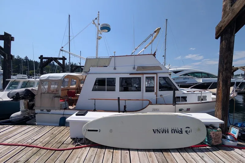 Slide: The Image of 1987 Island Gypsy 32 boat docked with a surfboard on the pier, under clear skies. - 35