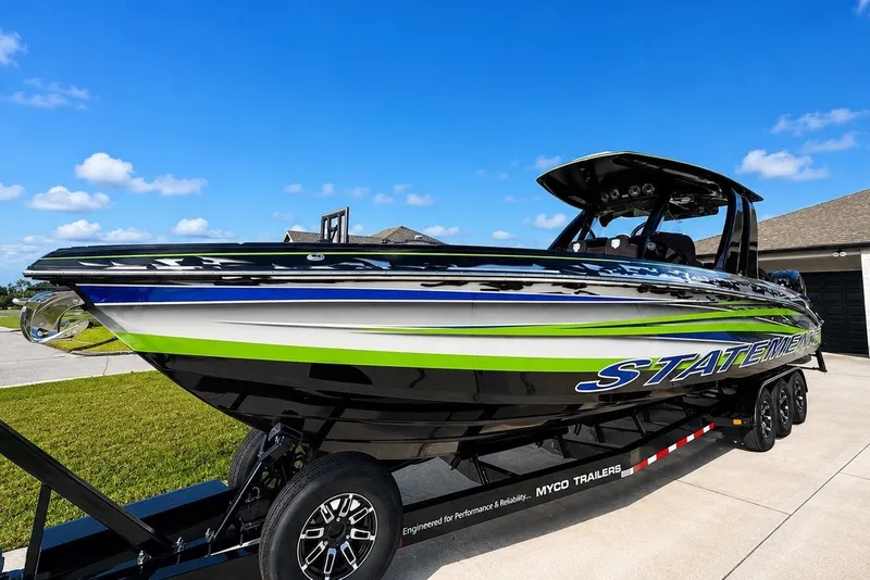 Slide: The Image of 2017 Statement 380 Open boat on trailer, vibrant green and blue design, clear sky background. - 13