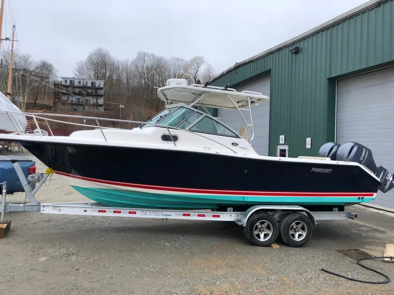 Slide: The Image of A 2016 Pursuit OS 255 Offshore boat on a trailer in front of a warehouse. - 0