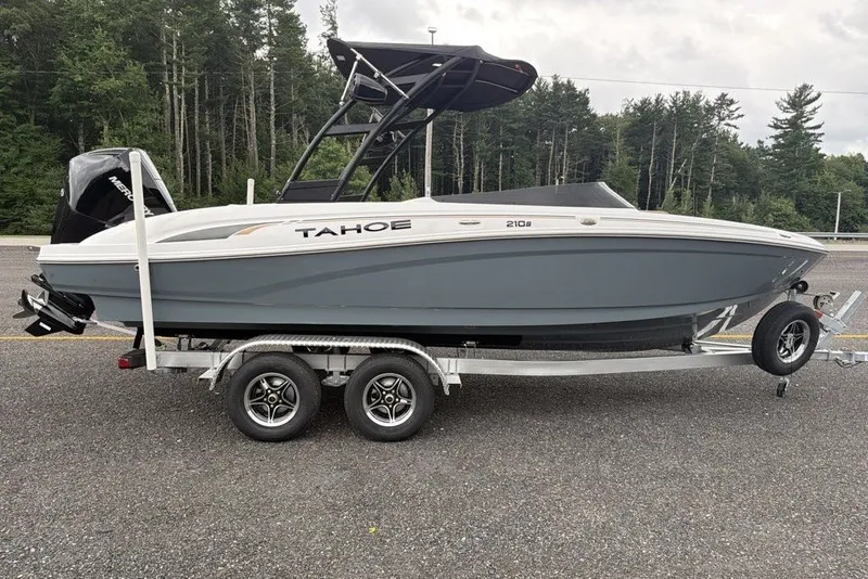 Slide: The Image of 2026 Tahoe 210 S boat on trailer, parked on asphalt, surrounded by trees. - 3