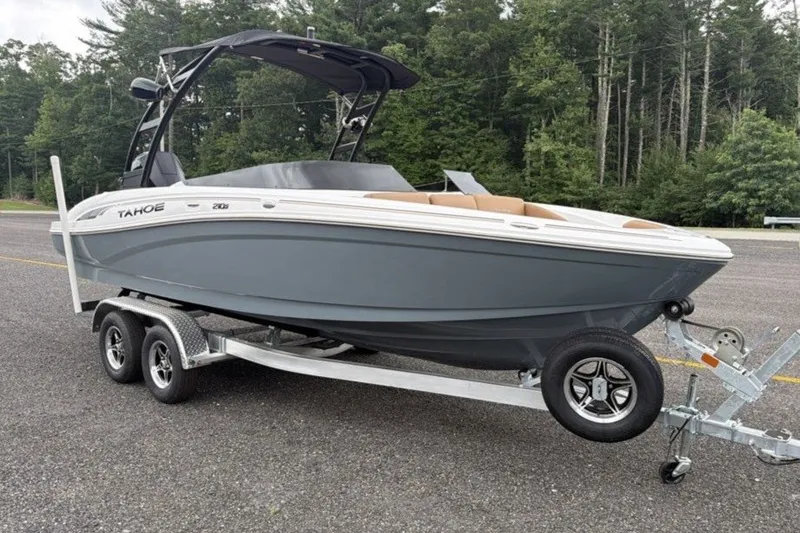 Slide: The Image of 2026 Tahoe 210 S boat on trailer, parked on asphalt, surrounded by trees. - 2