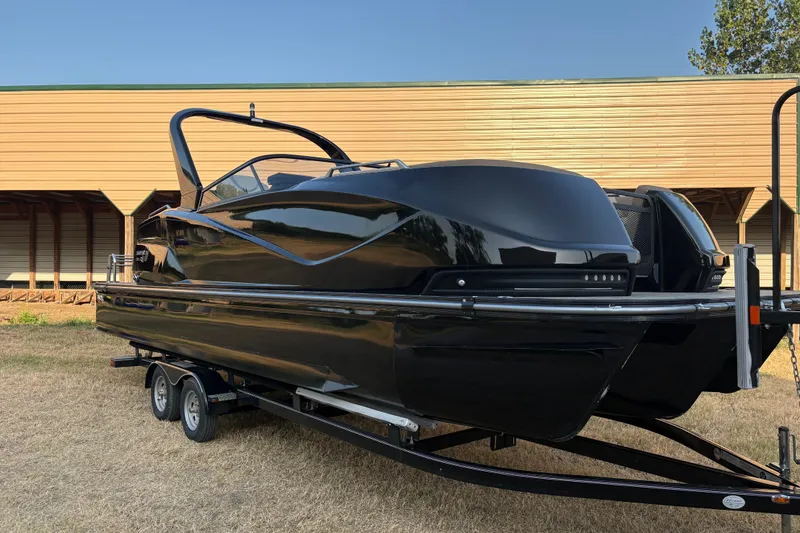 Slide: The Image of 2019 SunCatcher Amara boat on trailer, sleek black design, parked outdoors. - 2