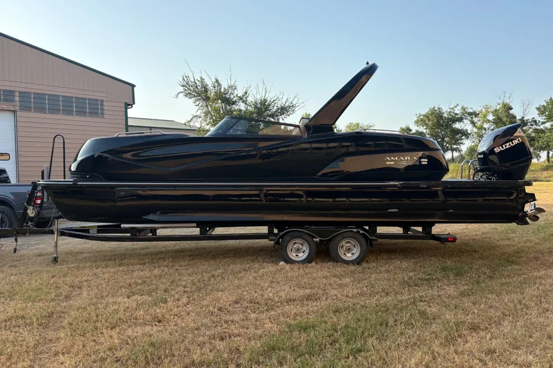Slide: The Image of Black 2019 SunCatcher Amara boat on trailer, parked outdoors near a building. - 6