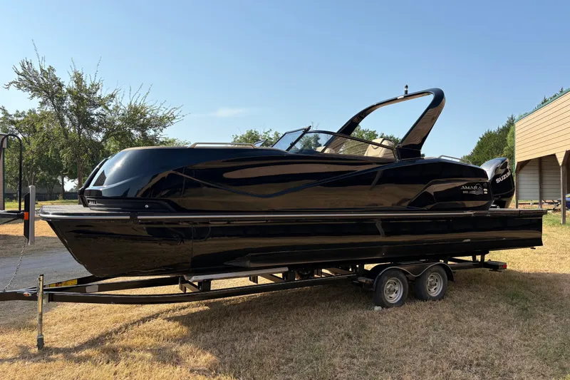 Slide: The Image of 2019 SunCatcher Amara boat on trailer, sleek black design, parked on grass. - 29