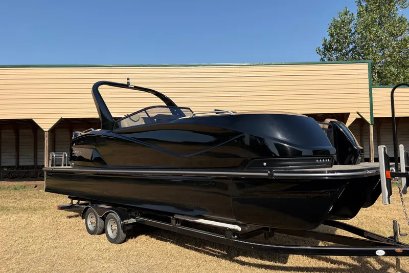 Slide: The Image of 2019 SunCatcher Amara boat on trailer, sleek black design, parked outdoors. - 26