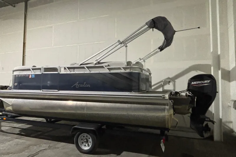 The Image of 2024 Avalon VLS Quad Lounge 19' pontoon boat with Mercury outboard motor in a garage. - 0