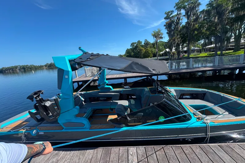 Slide: The Image of 2022 Nautique Super Air Nautique G23 boat docked by a serene lake under a clear blue sky. - 111
