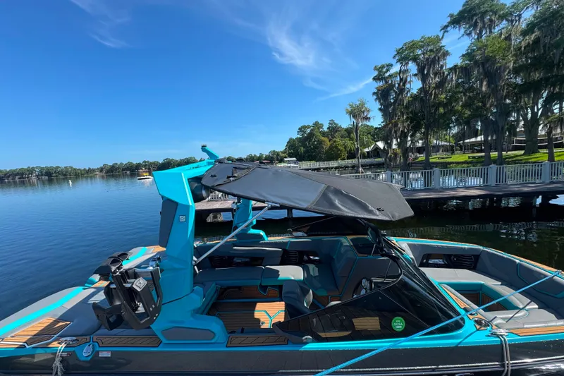 Slide: The Image of 2022 Nautique Super Air Nautique G23 boat docked on a serene lake under a clear blue sky. - 95