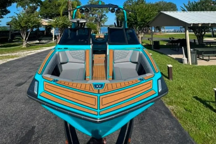 Slide: The Image of 2022 Nautique Super Air Nautique G23 boat with vibrant teal and wood accents, parked outdoors. - 5
