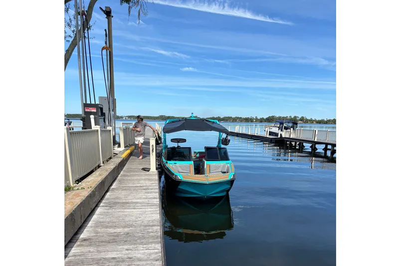 Slide: The Image of A turquoise 2022 Nautique Super Air Nautique G23 is docked at a wooden pier on a calm lake. - 29