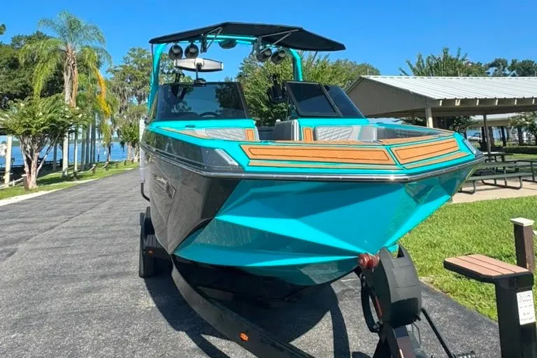 Slide: The Image of 2022 Nautique Super Air Nautique G23 boat in vibrant turquoise, parked near a lakeside pavilion. - 4