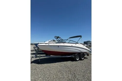 The Image of 2018 Yamaha Boats SX210 on trailer, parked on gravel under clear blue sky. - 0