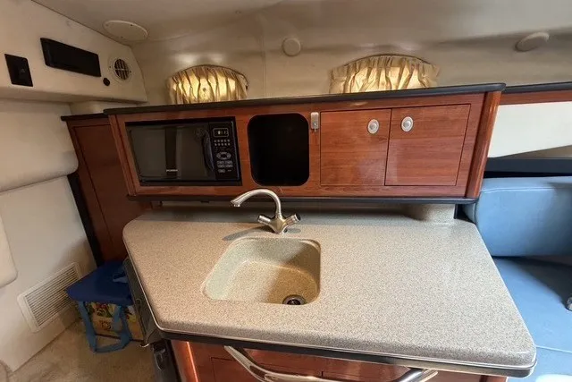 Slide: The Image of Interior of 2006 Sea Ray 270 Amberjack featuring kitchenette with sink, microwave, and wooden cabinets. - 16