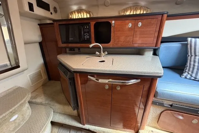 Slide: The Image of 2006 Sea Ray 270 Amberjack cabin with kitchenette, featuring wood cabinetry and compact appliances. - 15