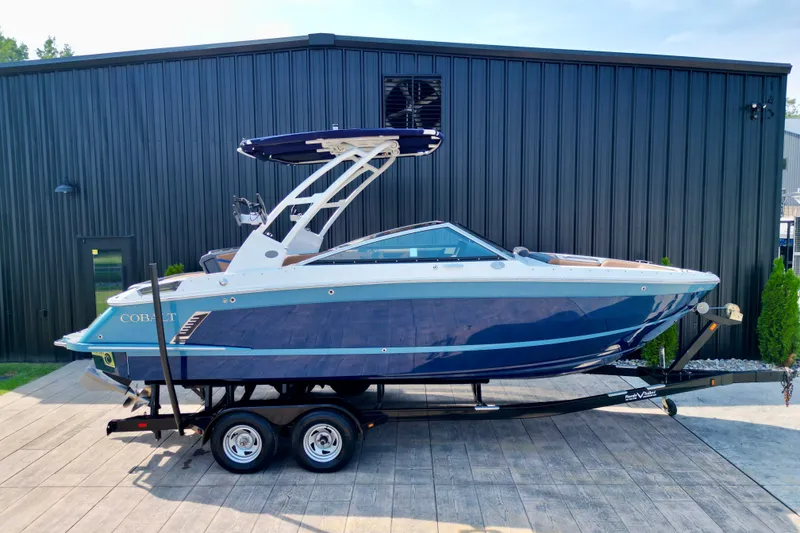 Slide: The Image of 2022 Cobalt R4 Surf boat on trailer, parked outside a black building. - 22