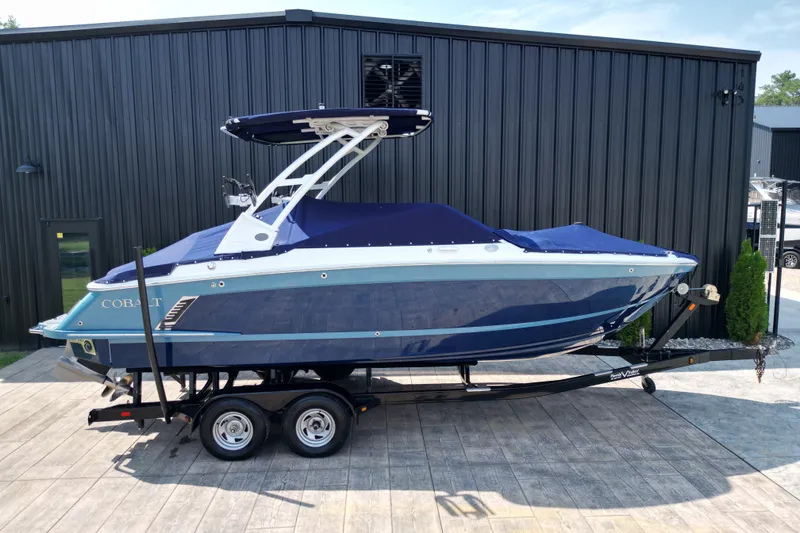 Slide: The Image of 2022 Cobalt R4 Surf boat on trailer, blue cover, parked outside black building. - 2