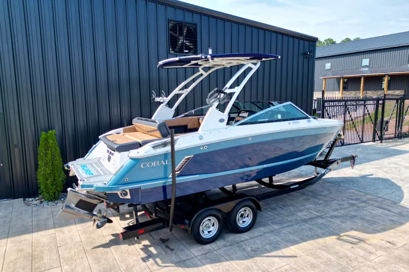 Slide: The Image of 2022 Cobalt R4 Surf boat on trailer, parked beside a modern building. - 20