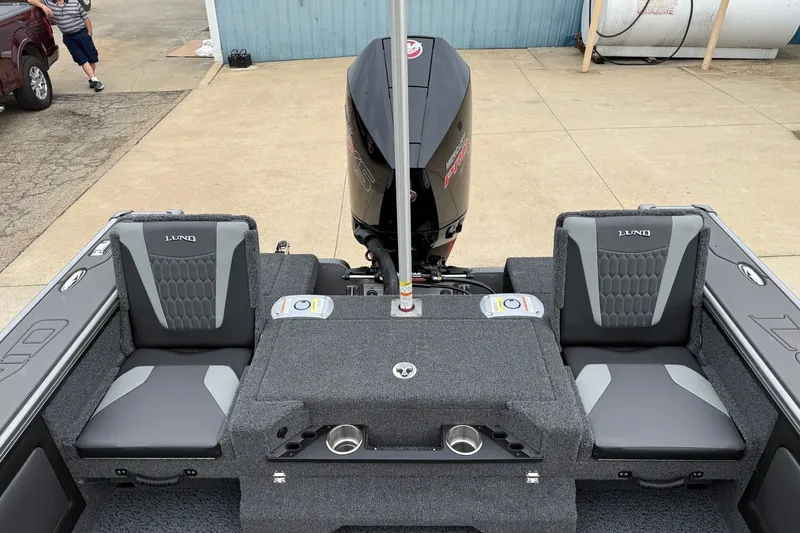 Slide: The Image of 2027 Lund 1975 Pro-V boat interior with dual seats and motor, parked on concrete. - 35