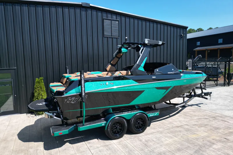Slide: The Image of 2027 Tigé 22RZX boat in teal and black, parked on a trailer beside a modern building. - 19
