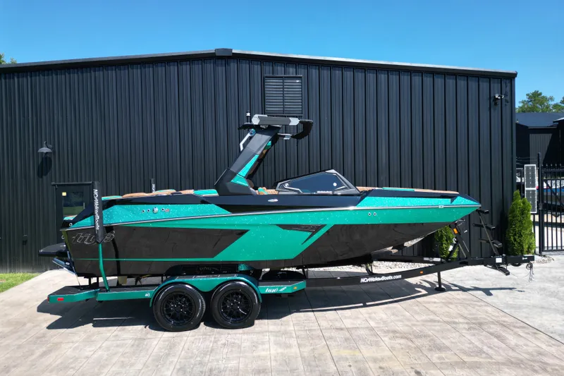 Slide: The Image of 2027 Tigé 22RZX boat in vibrant teal and black, parked on a trailer outside a black building. - 1