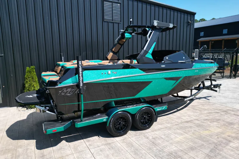 Slide: The Image of 2027 Tigé 22RZX boat in teal and black, parked on a trailer outside a building. - 2