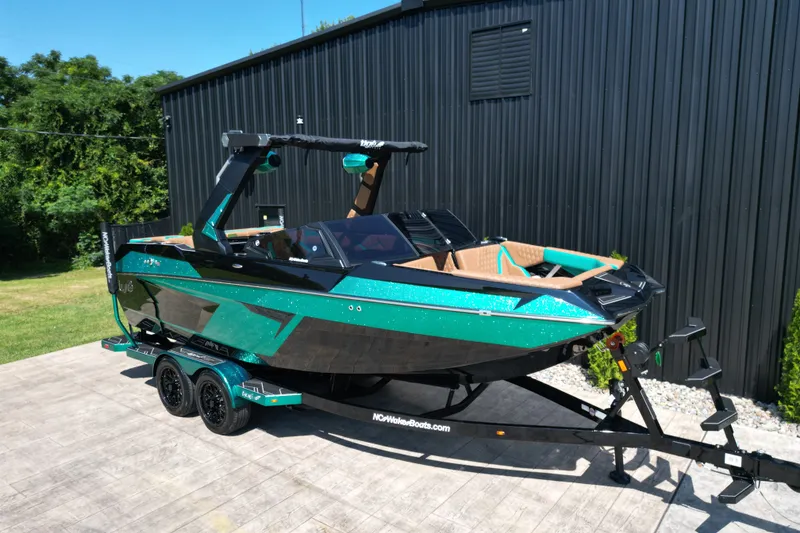 Slide: The Image of 2027 Tigé 22RZX boat in vibrant teal and black, parked on a trailer beside a black building. - 17