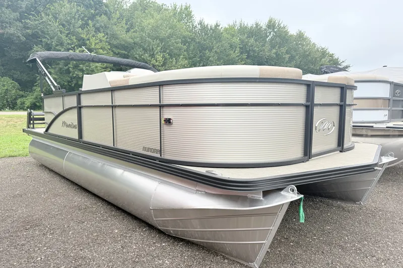 The Image of 2027 Manitou Aurora SE 21 pontoon boat parked on gravel with lush greenery background. - 1