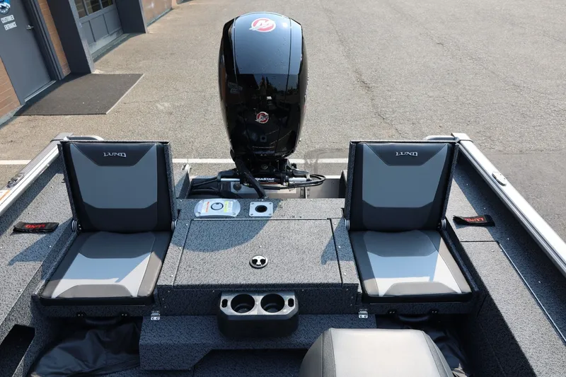 Slide: The Image of 2027 Lund 1875 Impact XS Sport boat interior with seating and motor, parked outdoors. - 41