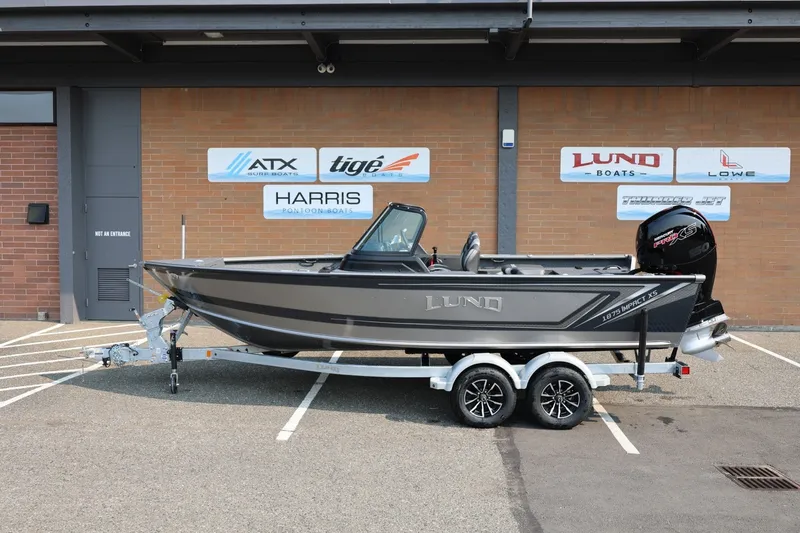 The Image of 2027 Lund 1875 Impact XS Sport boat on trailer, parked outside dealership. - 1