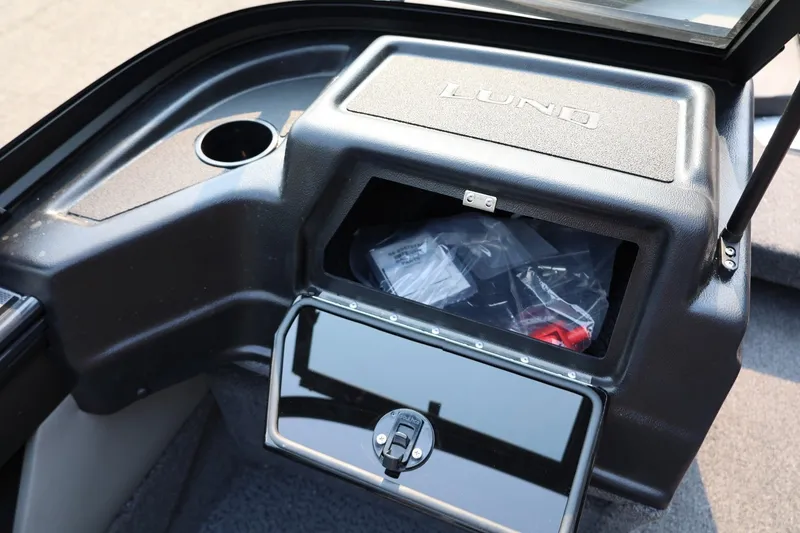 Slide: The Image of The image shows a storage compartment in a Lund 1875 Crossover XS boat with an open lid. - 28