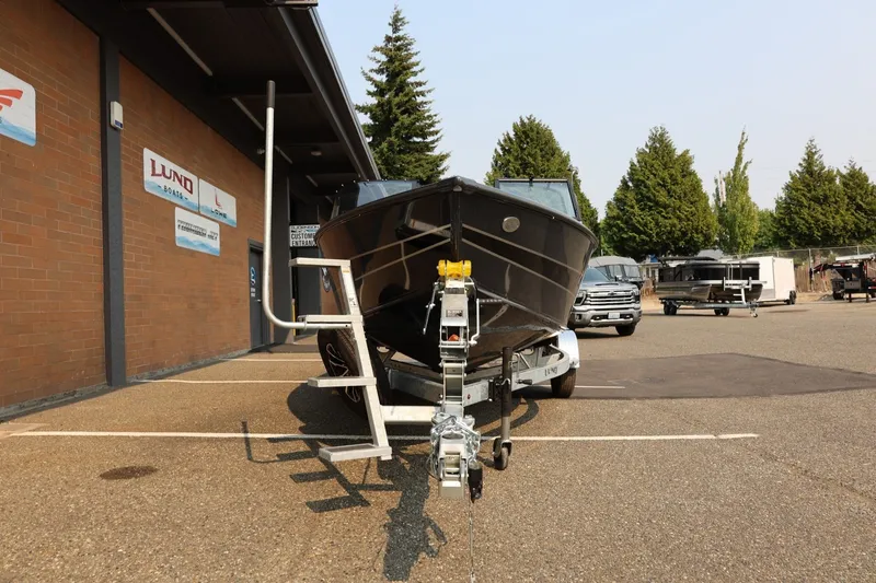 Slide: The Image of A Lund 1875 Crossover XS boat on a trailer in front of a building with trees in the background. - 12