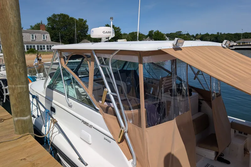 Slide: The Image of 2000 Pursuit 3400 Express boat docked, featuring tan canopy and clear windows. - 32