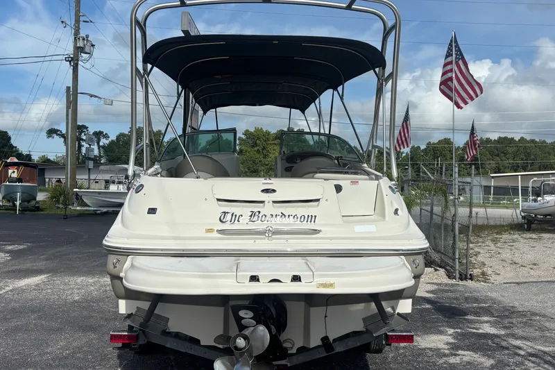 Slide: The Image of 2006 Sea Ray 240 Sundeck boat with canopy, parked outdoors, American flags in background. - 5
