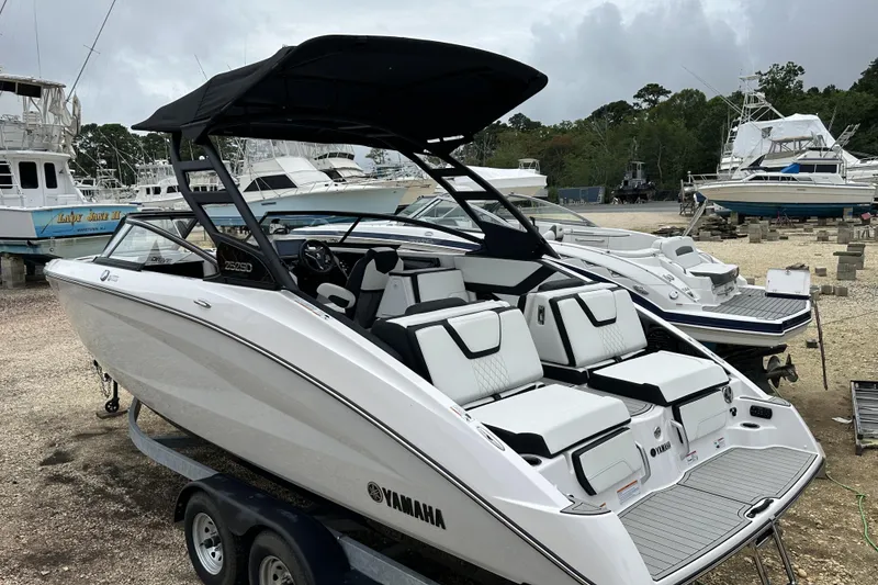Slide: The Image of 2025 Yamaha Boats 252SD on trailer, sleek design, white exterior, marina background. - 1