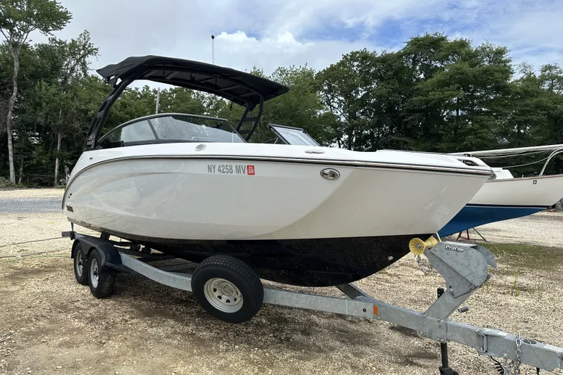 Slide: The Image of 2025 Yamaha Boats 252SD on trailer, parked outdoors, surrounded by trees. - 17