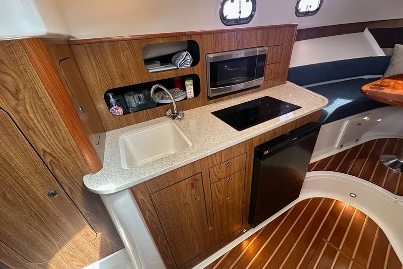Slide: The Image of 2013 Pursuit OS 345 Offshore yacht interior with kitchenette, featuring sink, stove, microwave, and wood cabinetry. - 18