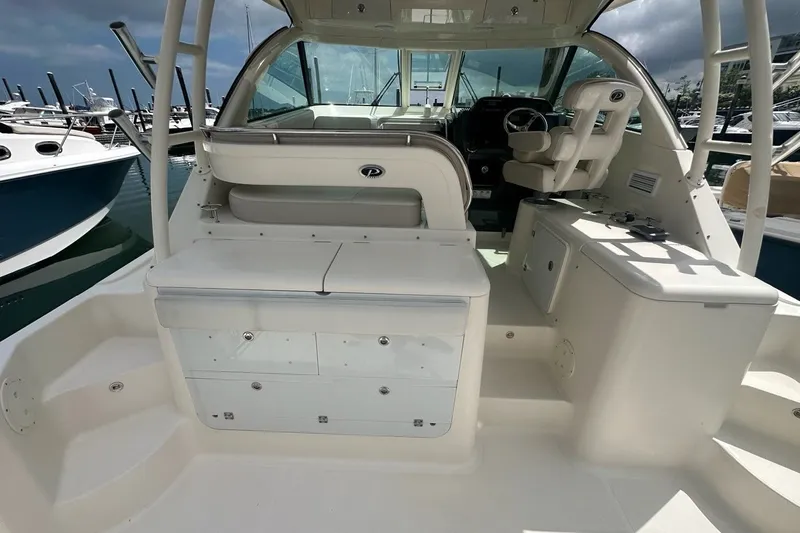Slide: The Image of 2013 Pursuit OS 345 Offshore boat interior, featuring helm and seating area at marina. - 27