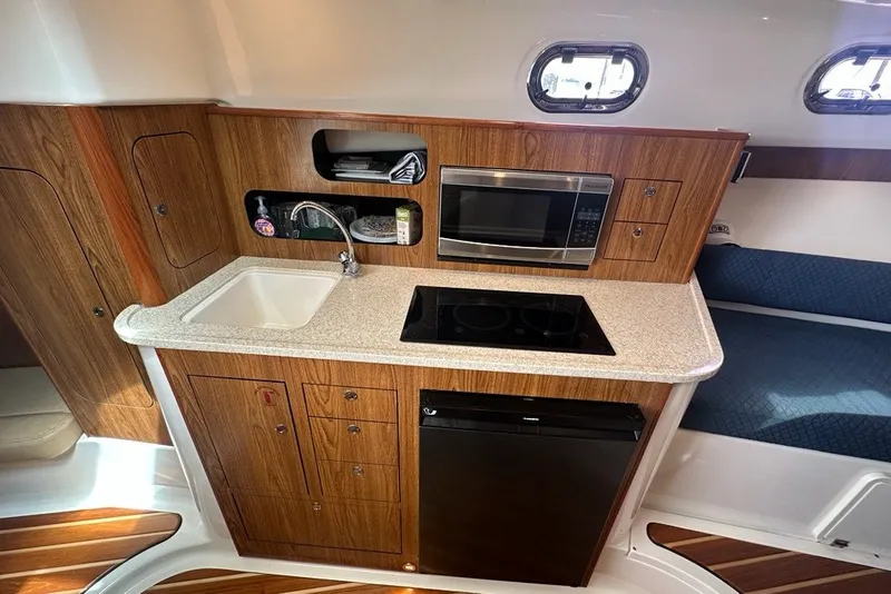 Slide: The Image of 2013 Pursuit OS 345 Offshore boat interior kitchen with sink, stove, microwave, and wood cabinetry. - 19