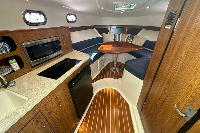 Slide: The Image of 2013 Pursuit OS 345 Offshore cabin interior with kitchenette, seating, and wooden accents. - 15