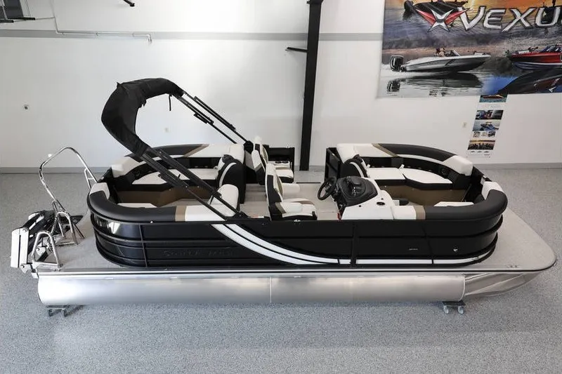 Slide: The Image of 2026 South Bay LE 224 pontoon boat in showroom, featuring sleek black and white design. - 2