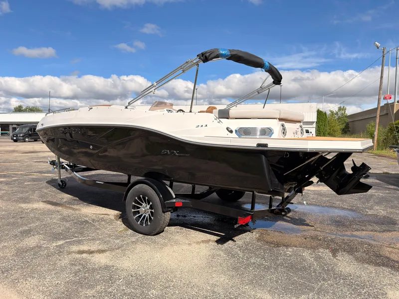 Slide: The Image of A 2027 Starcraft 211SVXIO boat on a trailer in a parking lot. It has a black hull and white top. - 5