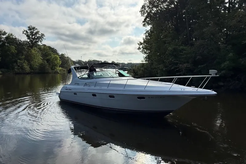 The Image of 1997 Cruisers Yachts 3375 Express on a serene river, surrounded by lush trees. - 0
