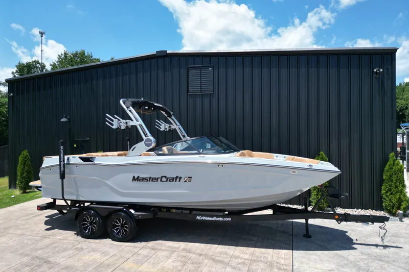 Slide: The Image of 2026 MasterCraft XT24 boat on trailer, parked outdoors against a black building. - 26