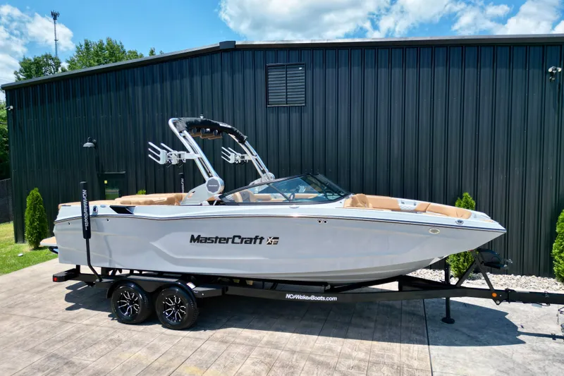 Slide: The Image of 2026 MasterCraft XT24 boat on trailer, parked outdoors near a black building. - 19