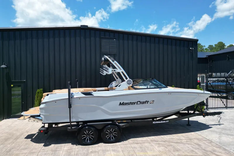 Slide: The Image of 2026 MasterCraft XT24 boat on trailer, parked outside a black building under a blue sky. - 27