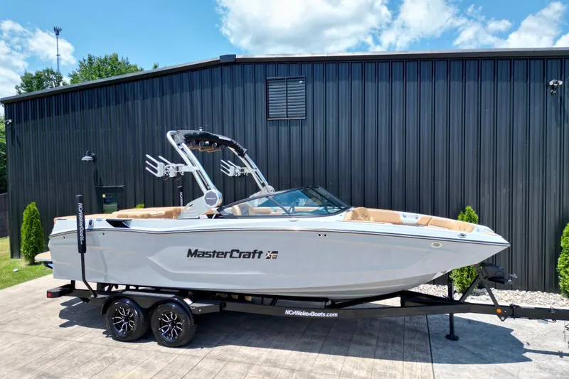 Slide: The Image of 2026 MasterCraft XT24 boat on trailer, parked outdoors against a black building. - 18